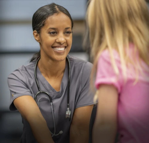 A medical professional in gray scrubs with a stethoscope smiling