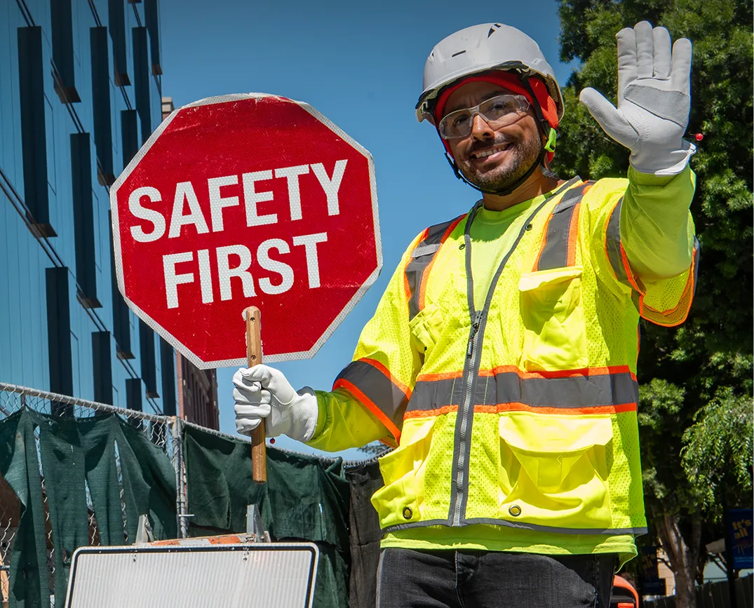 A smiling AWP Protector holding a red stop sign that says “Safety First.”