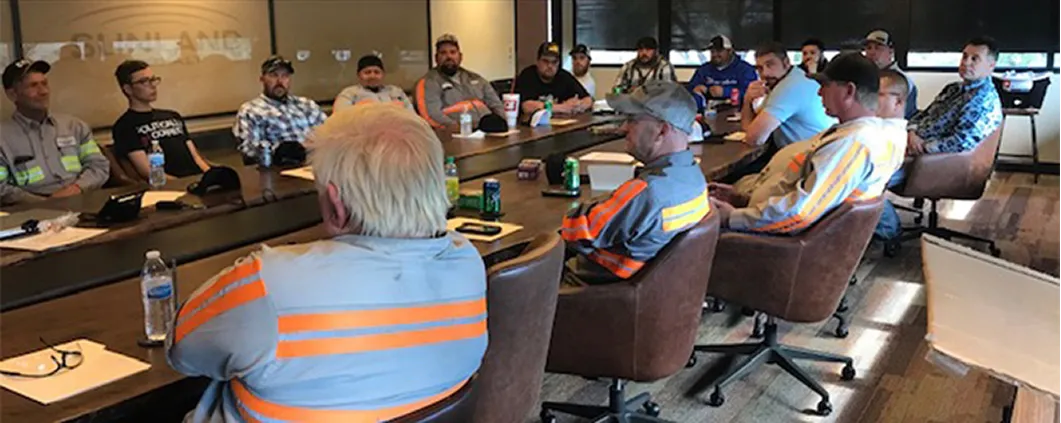 A group of employees sitting around a conference room desk at a safety meeting.