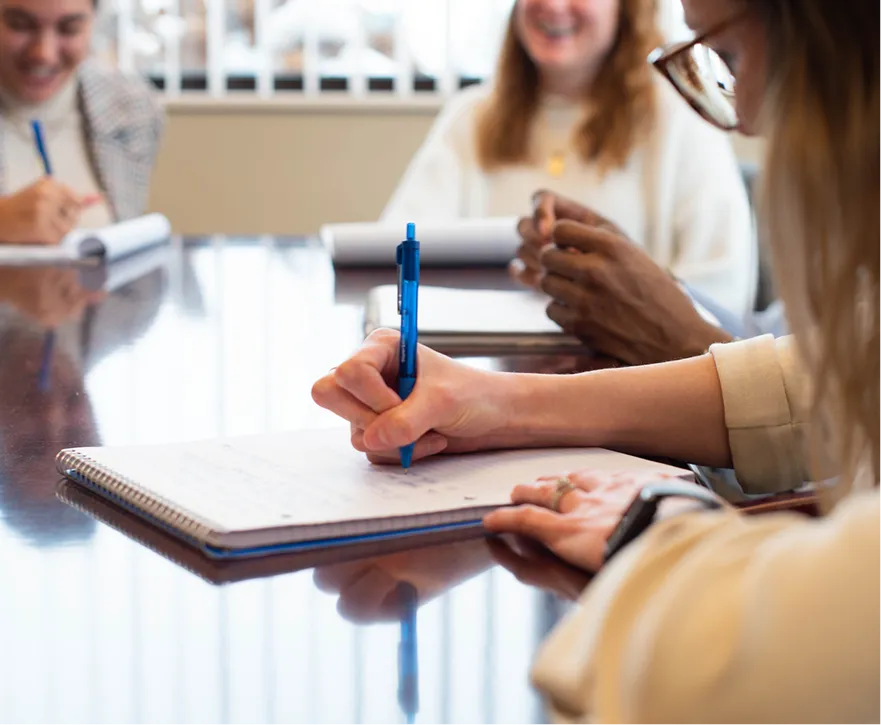 A group of interns laughing together and taking notes in a conference room.
