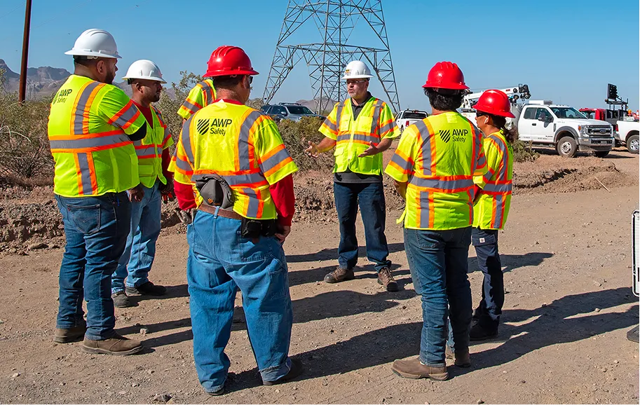 AWP employees in safety gear attending a meeting outdoors at a jobsite.