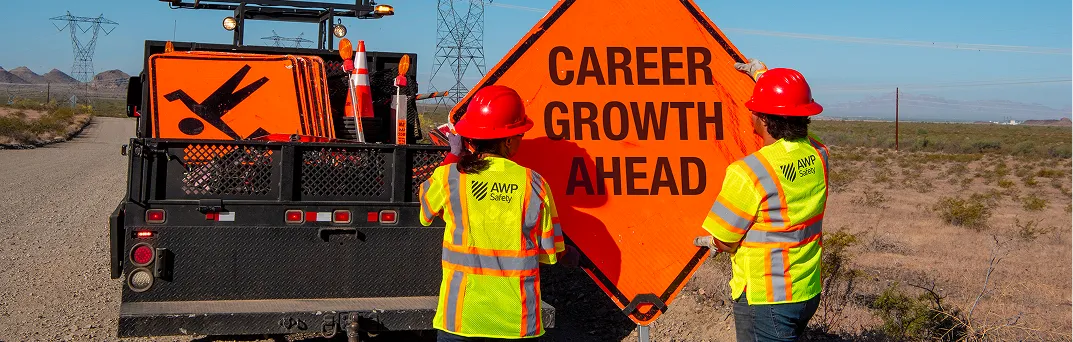 Two employees unloading an orange sign that says “Career Growth Ahead.”