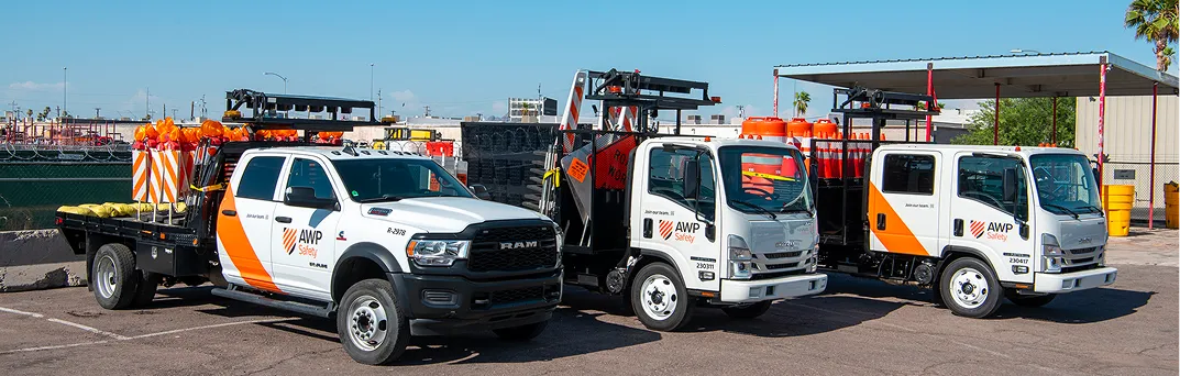 Three AWP work trucks loaded with traffic control signs, lights, cones, and sandbags.