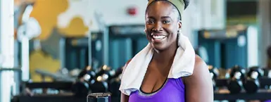 A smiling Black female employee works out with dumbbells at a CareerSource fitness facility (mobile).