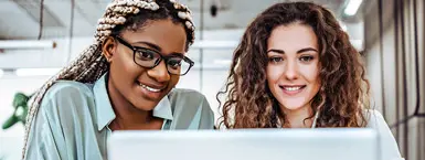 Two female employees study a computer screen in an office setting. (mobile)