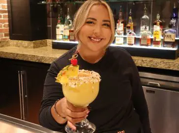 A Cheddar’s team member smiling and holding a mixed drink.