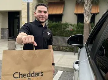 A Cheddar's team member smiling and holding a take-out bag.