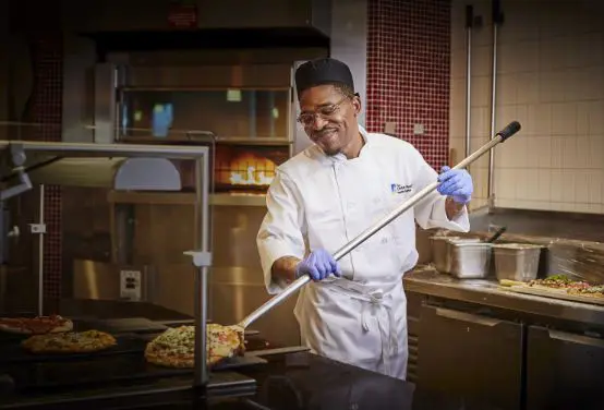 A Christ Hospital employee smiling as he cooks pizza.