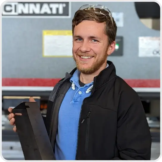 A smiling employee holding a metal part at Cincinnati Incorporated.