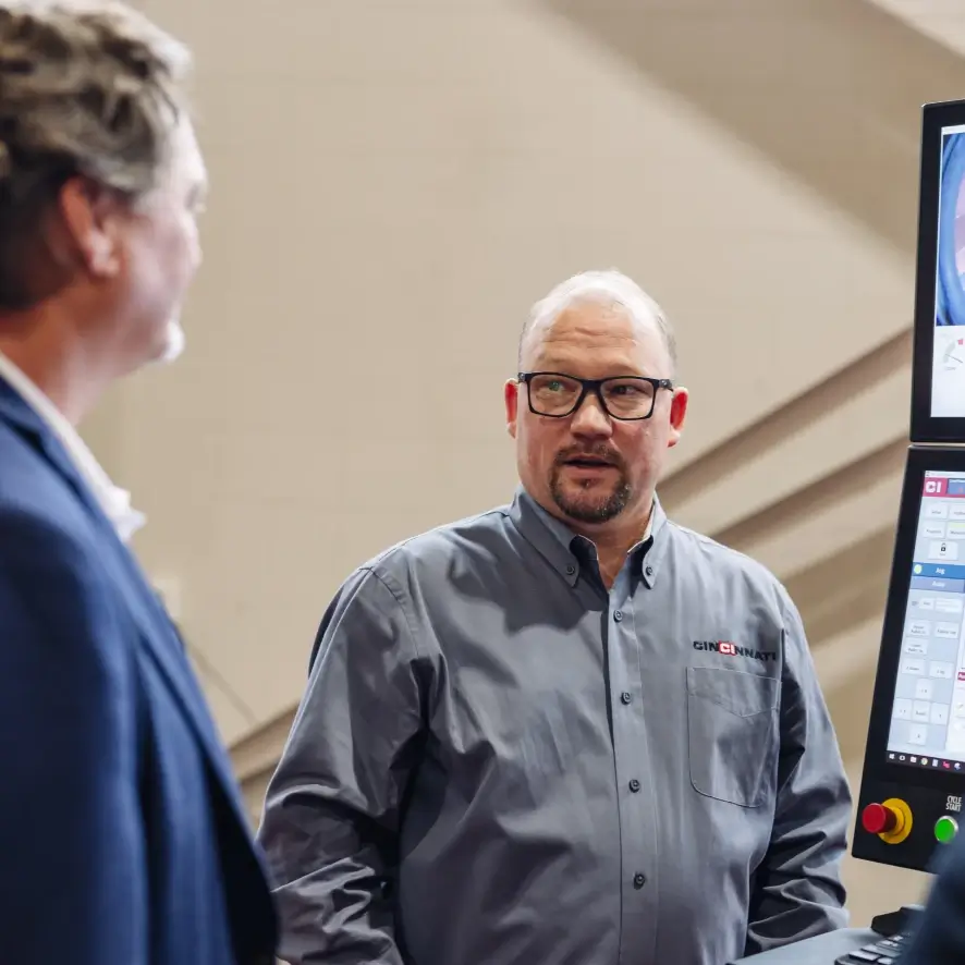 A Cincinnati Incorporated professional looking at a fellow colleague next to a computer.