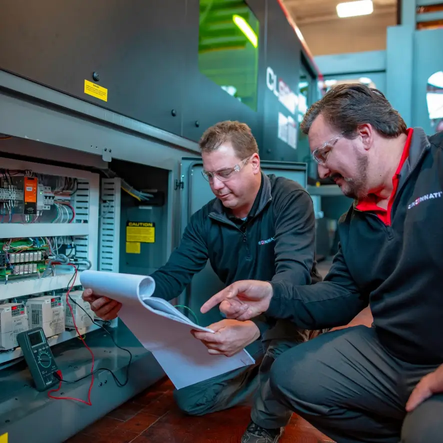 Two Cincinnati Incorporated employees kneeling together reviewing a manual.