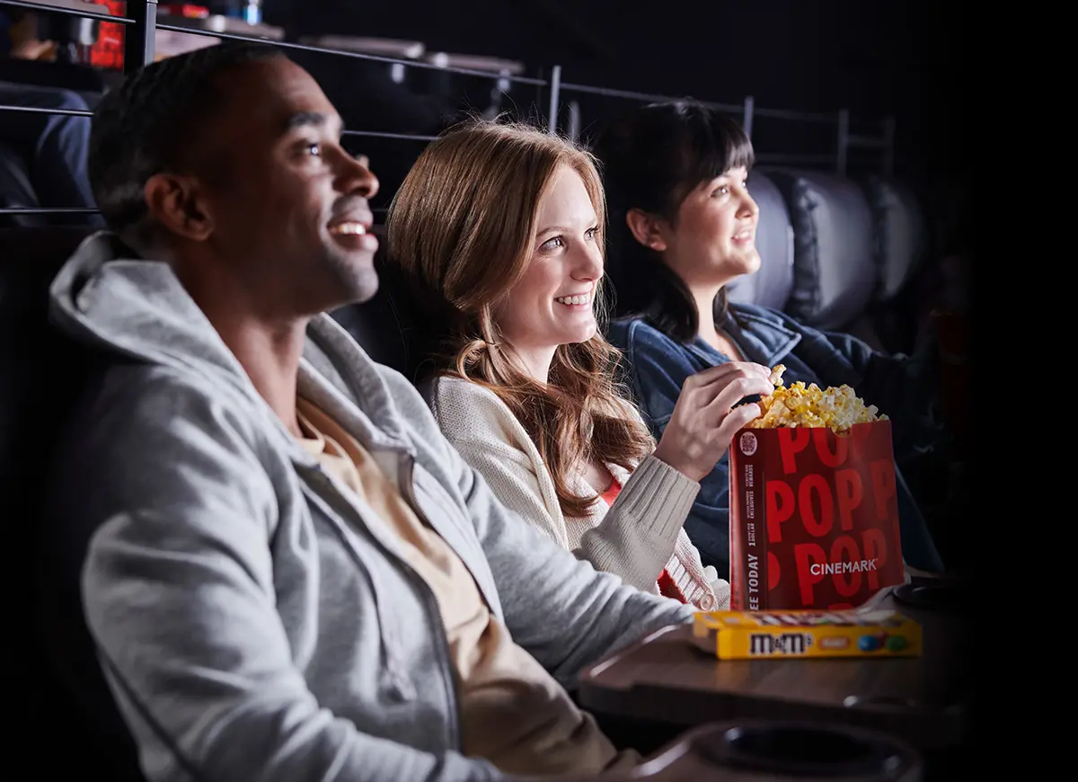 Three people watching a movie at a Cinemark theatre and eating popcorn.