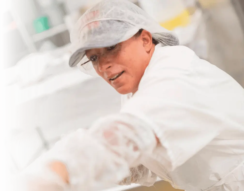An employee wearing white, protective head covering, goggles and a white gown arranges produce for delivery.