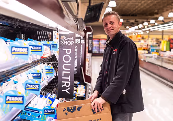 A Dierbergs associate standing and smiling while restocking chicken breast