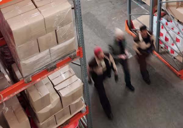 An aerial view of pallets in a warehouse above three employees walking side-by-side