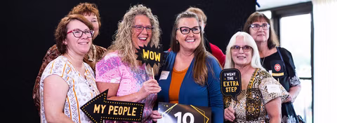 Seven Dierbergs associates smiling with silly photo prop signs