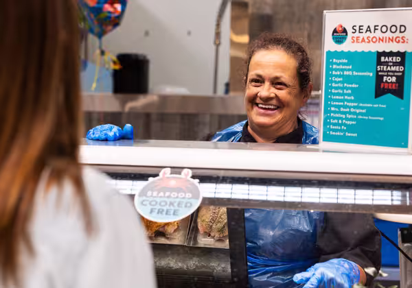 A deli/seafood employee standing behind a counter and smiling