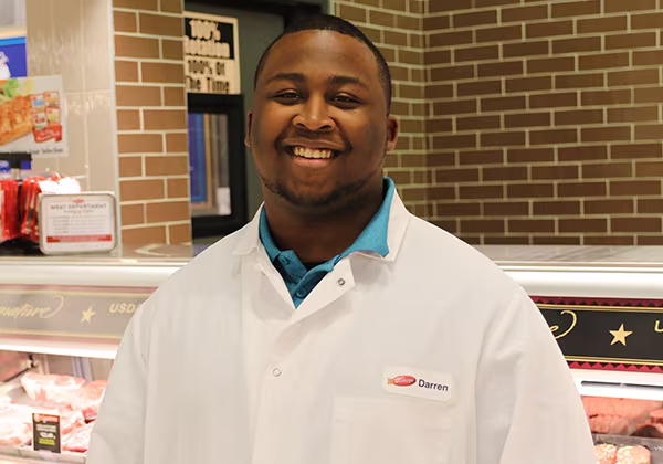 A Dierbergs meat department team member standing in front of a service counter and smiling