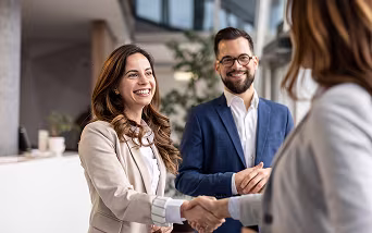 Three employees talking with one another and smiling while two shake hands.