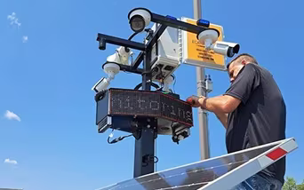 An ECAM field employee standing in a paved lot while installing monitoring equipment.