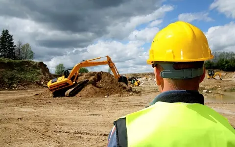 A person with hard hat on looking at an excavator.