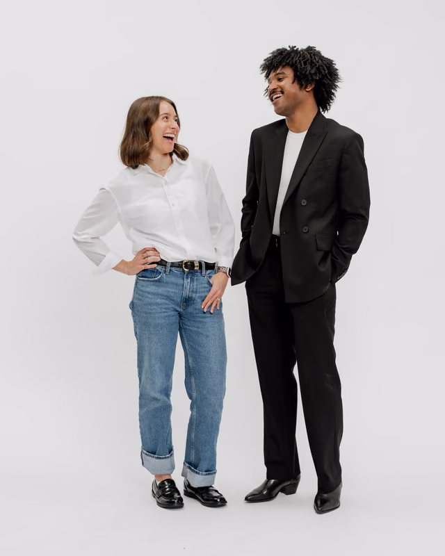 Two smiling Express associates standing side by side, a woman in a white shirt and jeans and a man in a black suit, laughing together against a light background.