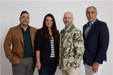 Group of four professionally dressed people standing and smiling against a white background.