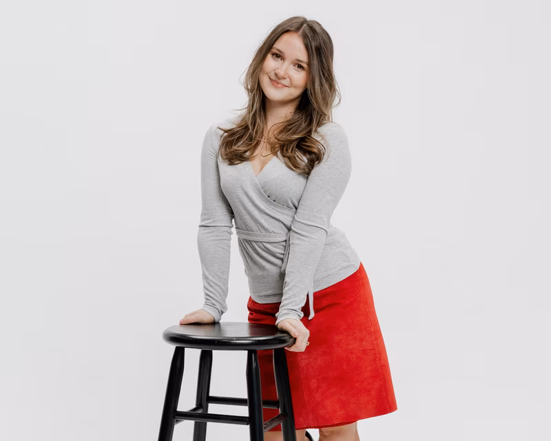 An Express grad student leaning on a chair and smiling.