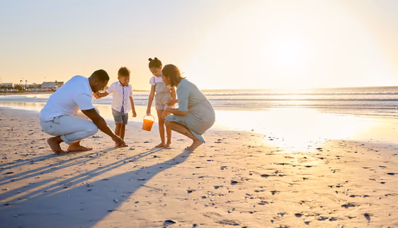 A happy family collecting shells on a beach at sunset.