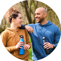 A smiling couple talking outdoors, one holding a water bottle.