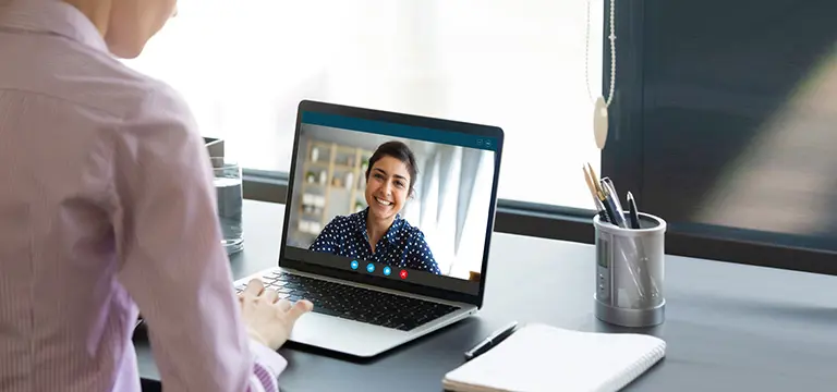 A telehealth counselor conducting a virtual meeting session with her client smiling on screen.