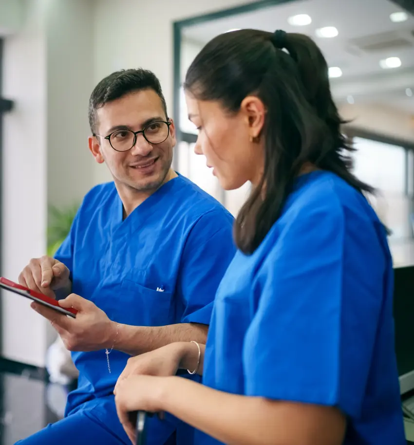 A dentist smiling while engaged in conversation with a dental assistant.