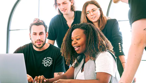 A small group of marketing employees crowd around a laptop sharing ideas on a project.