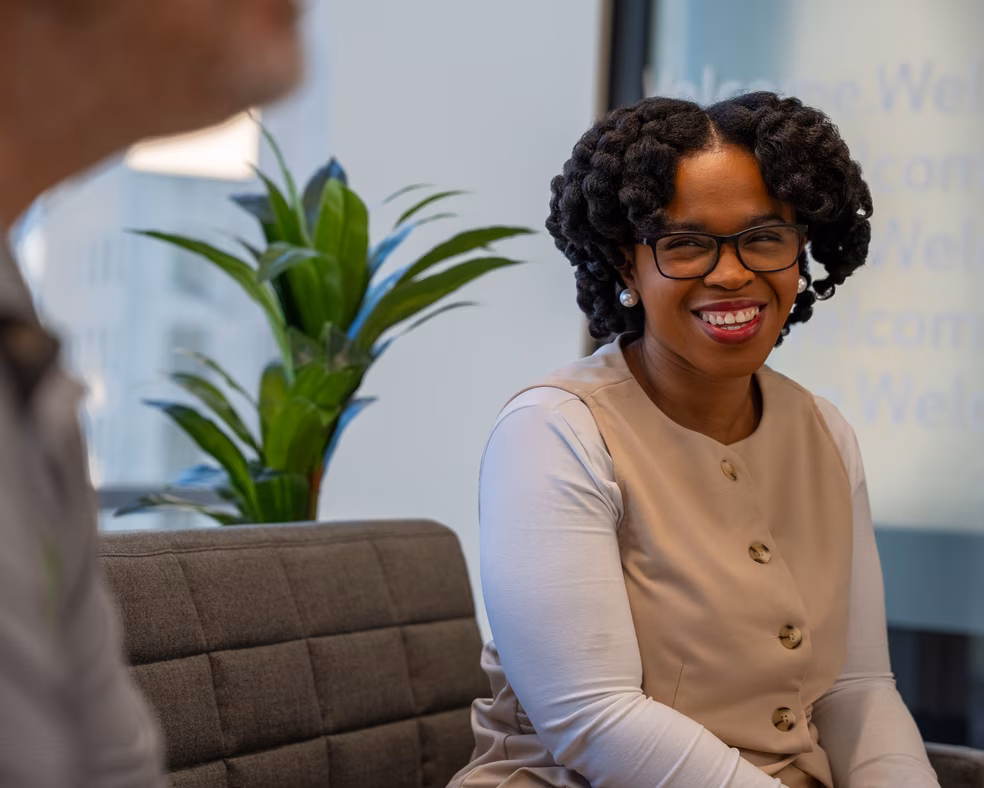 A woman wearing glasses and a brown shirt sits comfortably on a couch.