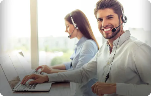 A call center agent wearing a headset and smiling as they work on a laptop.