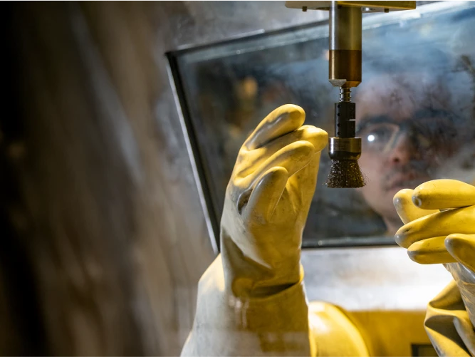 LANL worker using gloves to handle a cylindrical tool in a controlled workspace.