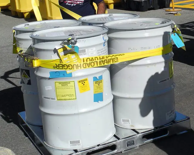A group of 55-gallon, gray metal drums containing hazardous waste.