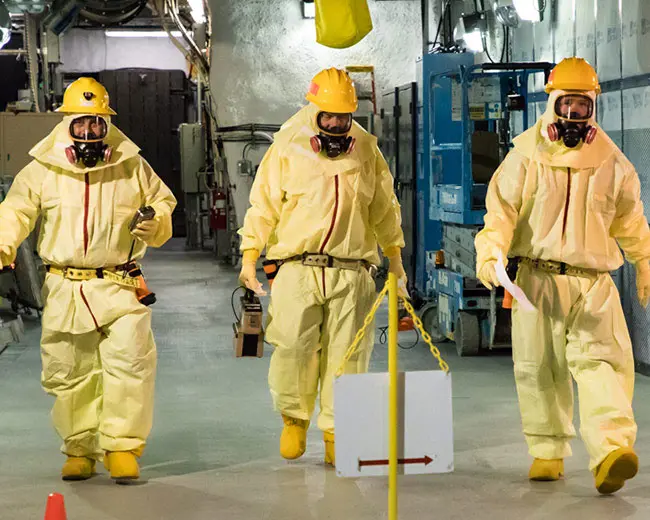 Three technicians in yellow hazmat suits.
