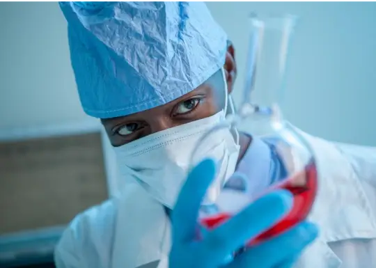 A doctor looking at red fluid in a round bottom flask.