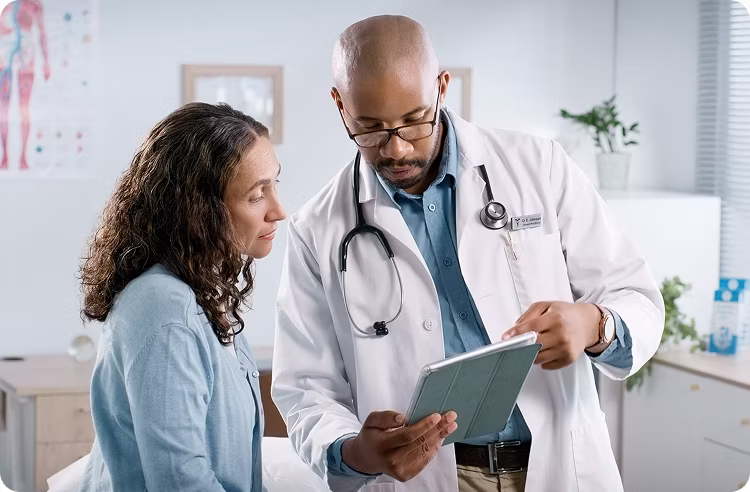 MRG Exams clinician with an electronic tablet speaking with a patient in an exam room.