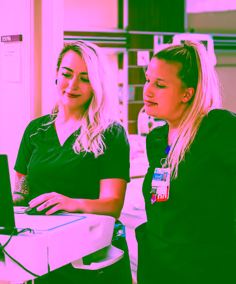 two nurses working together, looking at a computer screen