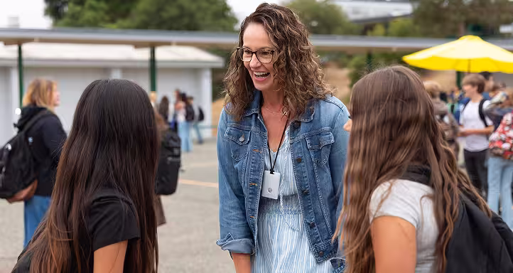 A teacher talking happily with two students outside.