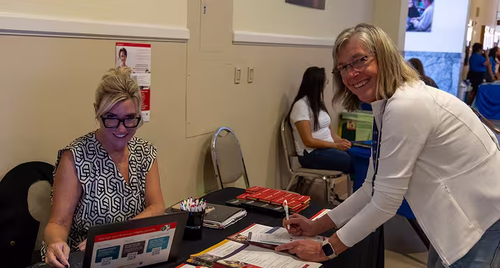 Two women on either side of a table, smiling for the camera.