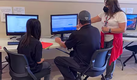 Three people sitting at a table, facing a computer.