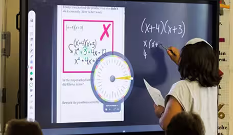 A teacher facing a smart board, writing a math equation.
