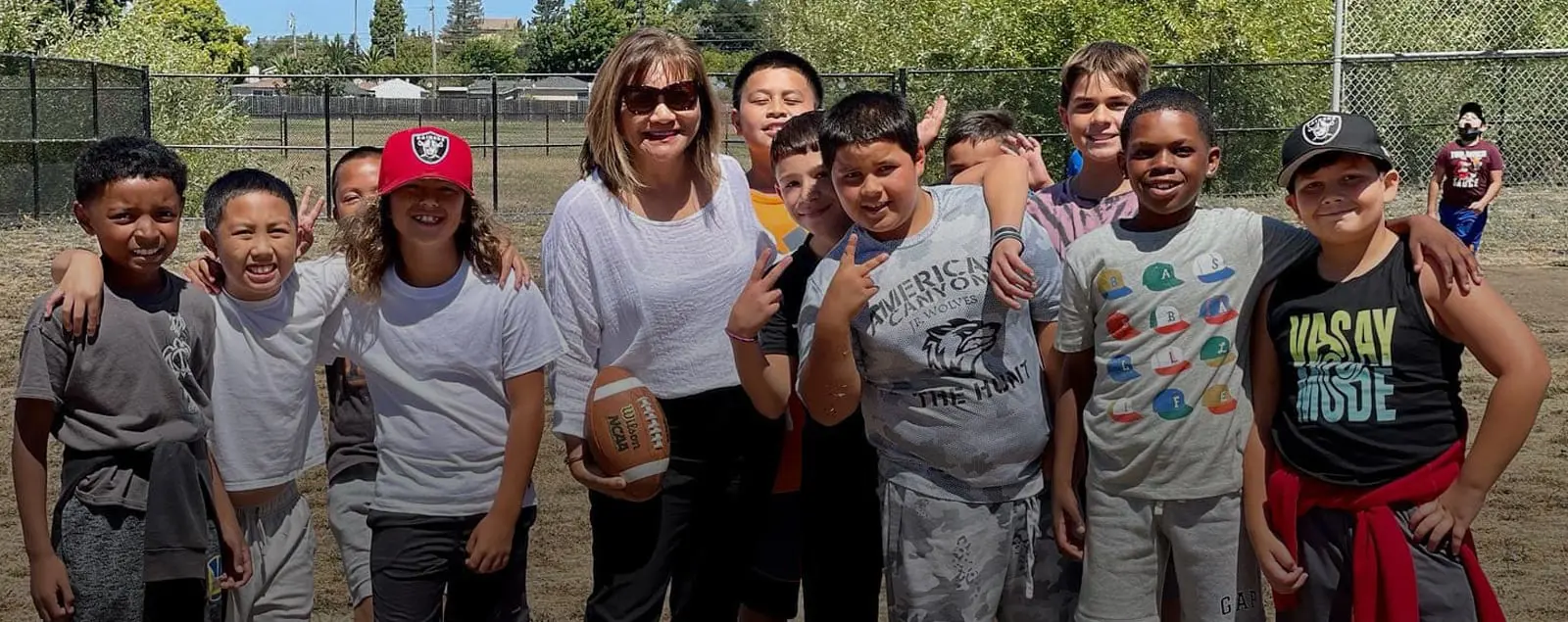 Employee holding a football and smiling with a group of students