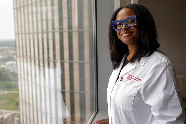 A physician in a lab coat stands by a window, looking thoughtfully outside.