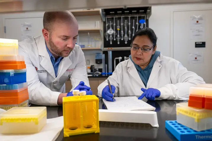 Two researchers in lab coats collaborating on a project at a laboratory workstation.