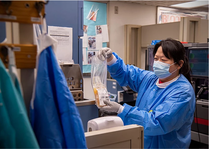 A medical professional handling a bag of plasma in a clinical laboratory.