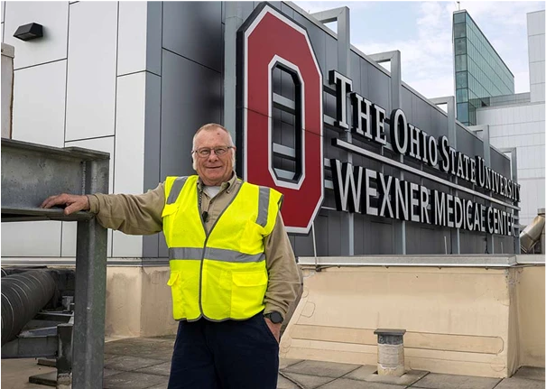 A facilities employee next to the OSU Wexner Medical Center roof sign.